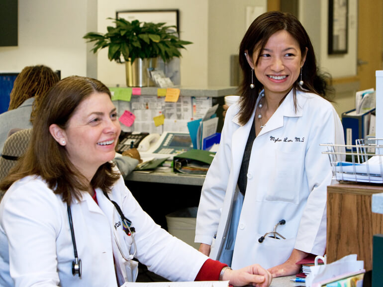 Two female physicians talking and smiling at the nurses station.