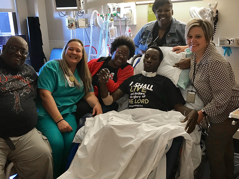 DeAndre sitting up in bed and surrounded by his family and members of his care team.