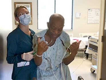 Herman signals he's OK with a double thumbs-up signal standing with his walker and a nurse.