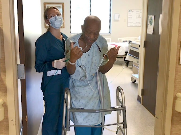 Herman gives a double thumbs-up signal standing with his walker and a nurse.